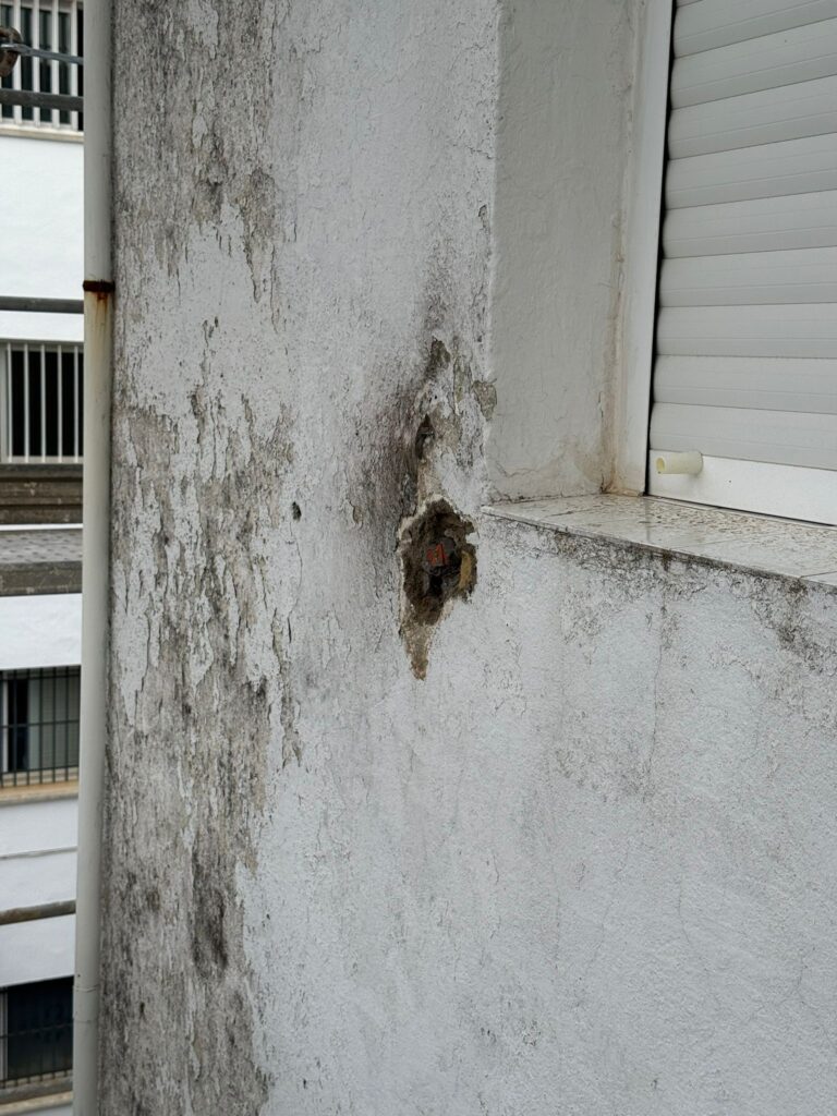 Desconchón en el paramento junto a una ventana, con la armadura oxidada a la vista y manchas de humedad, una de las patologías recogidas en la ITE