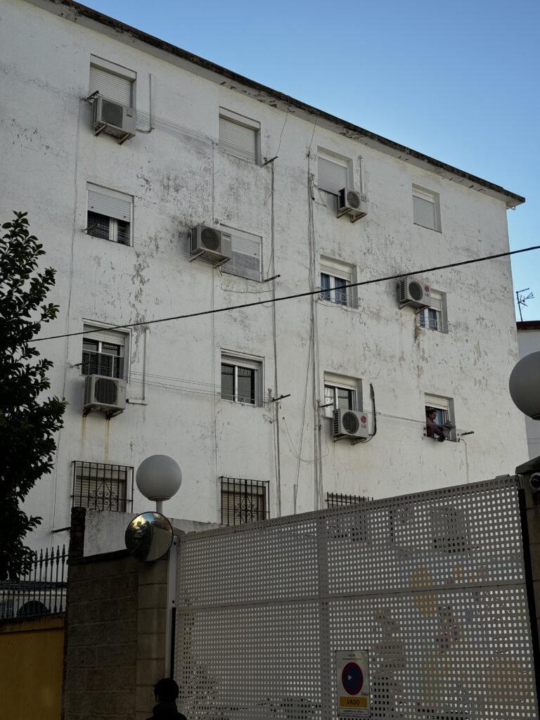 Fachada del bloque Manzana 4 antes de la rehabilitación energética en Sevilla, con la pintura descascarillada y aparatos de aire acondicionado colgados de las ventanas