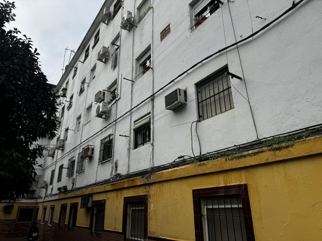 Fachada lateral del bloque con el zócalo amarillo, el cableado grapado en superficie y las máquinas de aire acondicionado sin ordenar